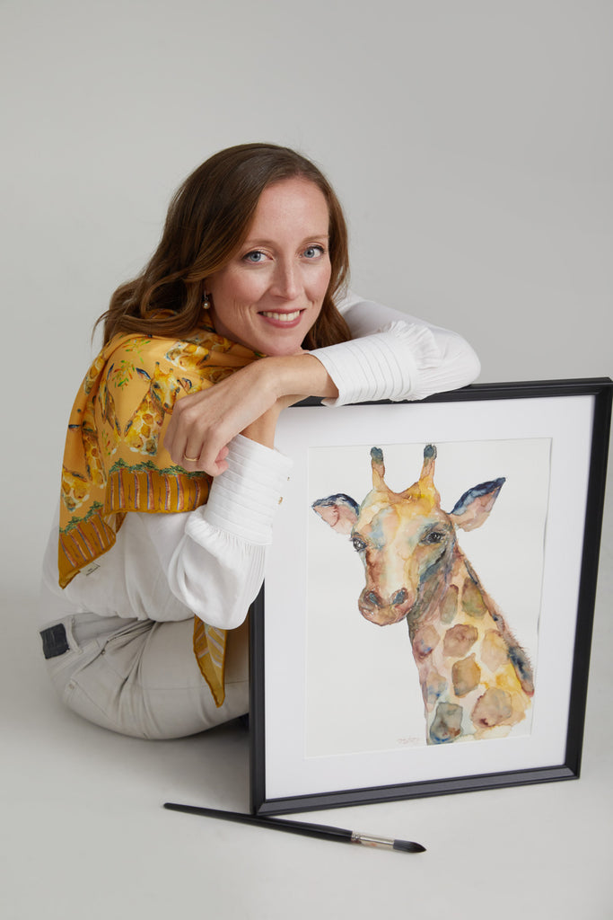 Artista diseñadora con cuadro enmarcado de jirafa en acuarela 