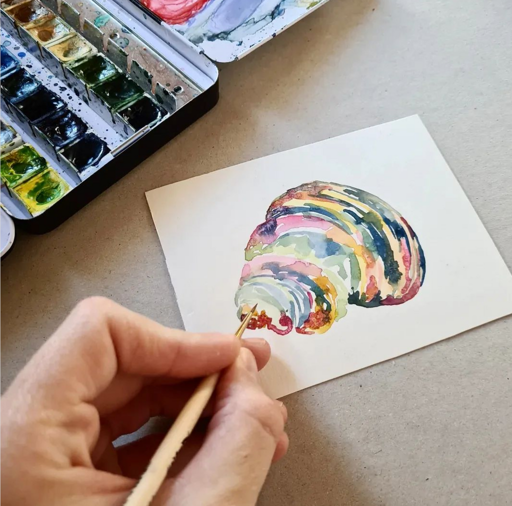 Detalle de mano con pincel pintando caracola de colores en acuarela 