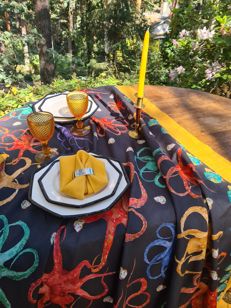 Mesa puesta en el jardín con mantel negro de algodón y lino con pulpos de colores y marco amarillo