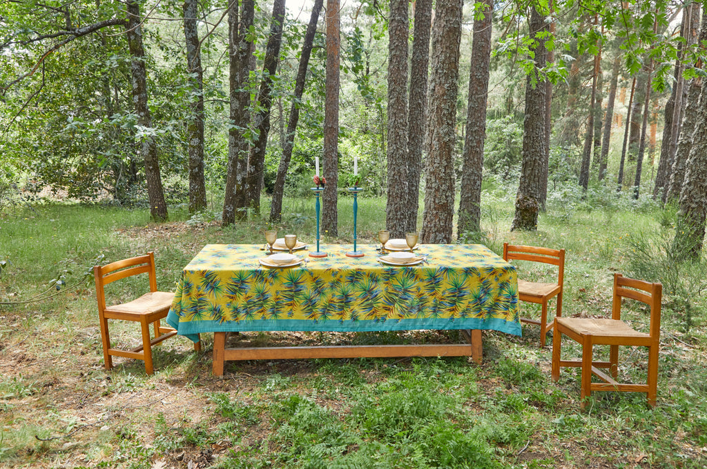Mesa en el jardín preparada para cuatro con mantel de lino y algodón color amarillo con marco turquesa