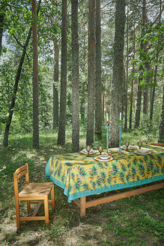 Detalle mesa puesta en el bosque con mantel de lino y algodón amarillo con hojas verdes