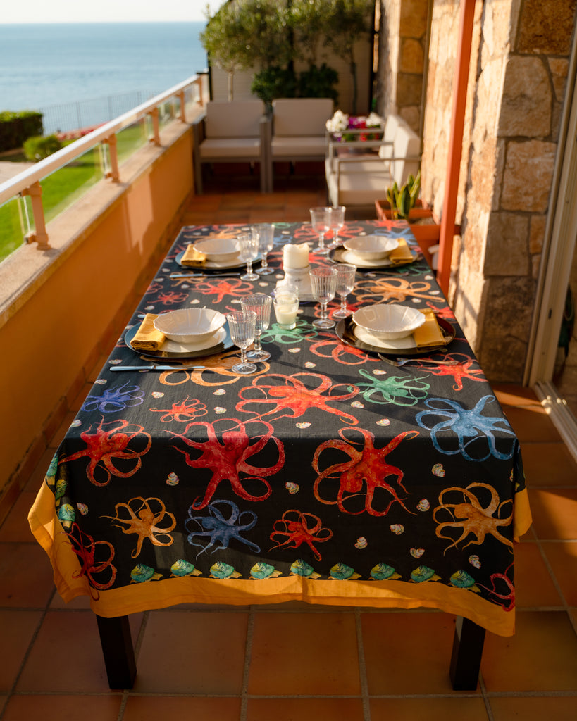 Mesa alargada en terraza con mantel de lino y algodón negro con diseños de animales marinos