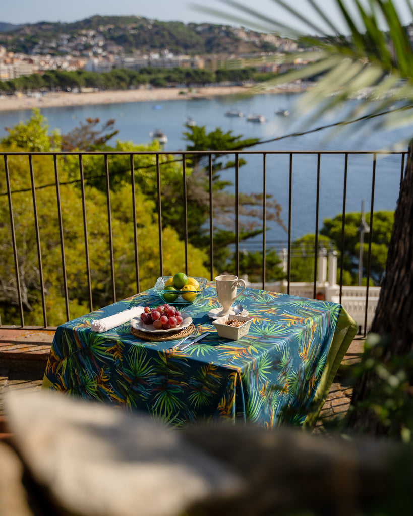 Terraza con vistas al mar y mesa decorada con mantel de algodón y lino azul con hojas verdes
