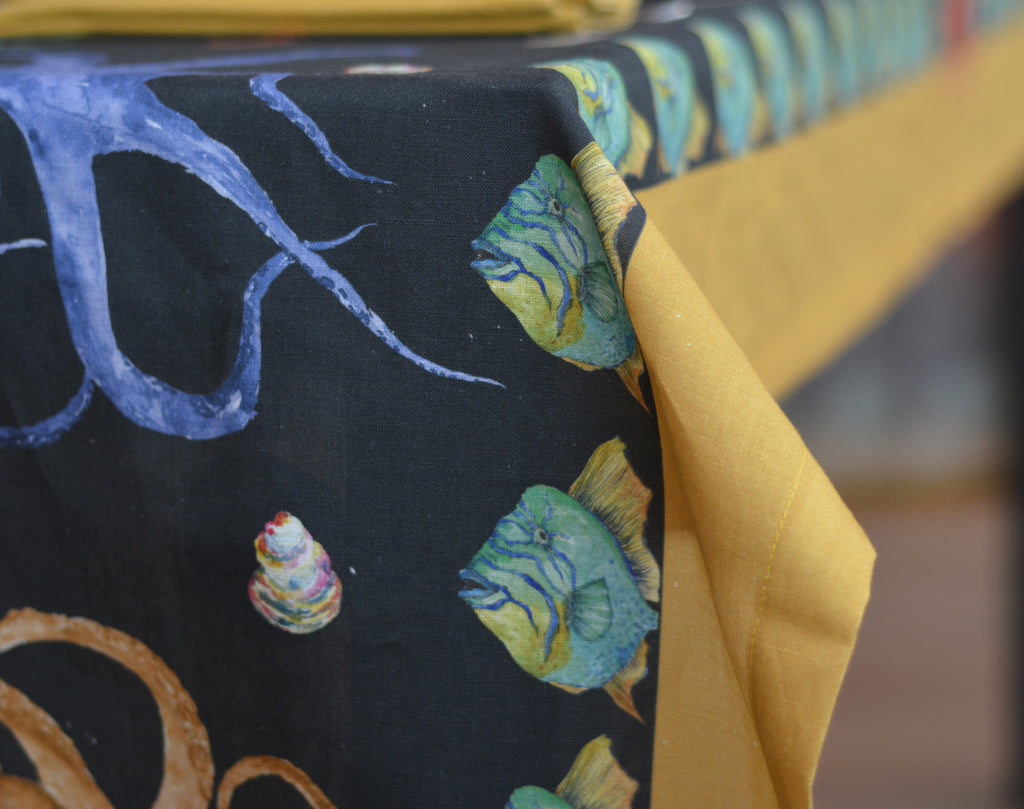 Detalle de mantel negro de algodón y lino con diseños de peces, pulpos y caracolas de colores, con franja amarilla