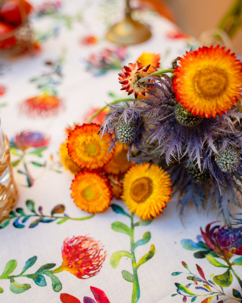 Detalle decoración de mesa con flores sobre mantel de lino y algodón blanco con diseños de proteas