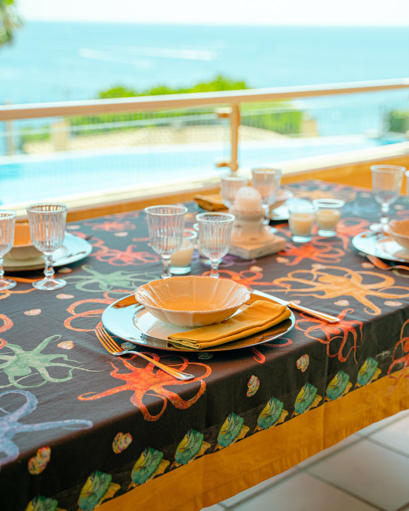 Detalle de mesa en terraza decorada con mantel de lino y algodón negro con diseños de animales marinos de colores
