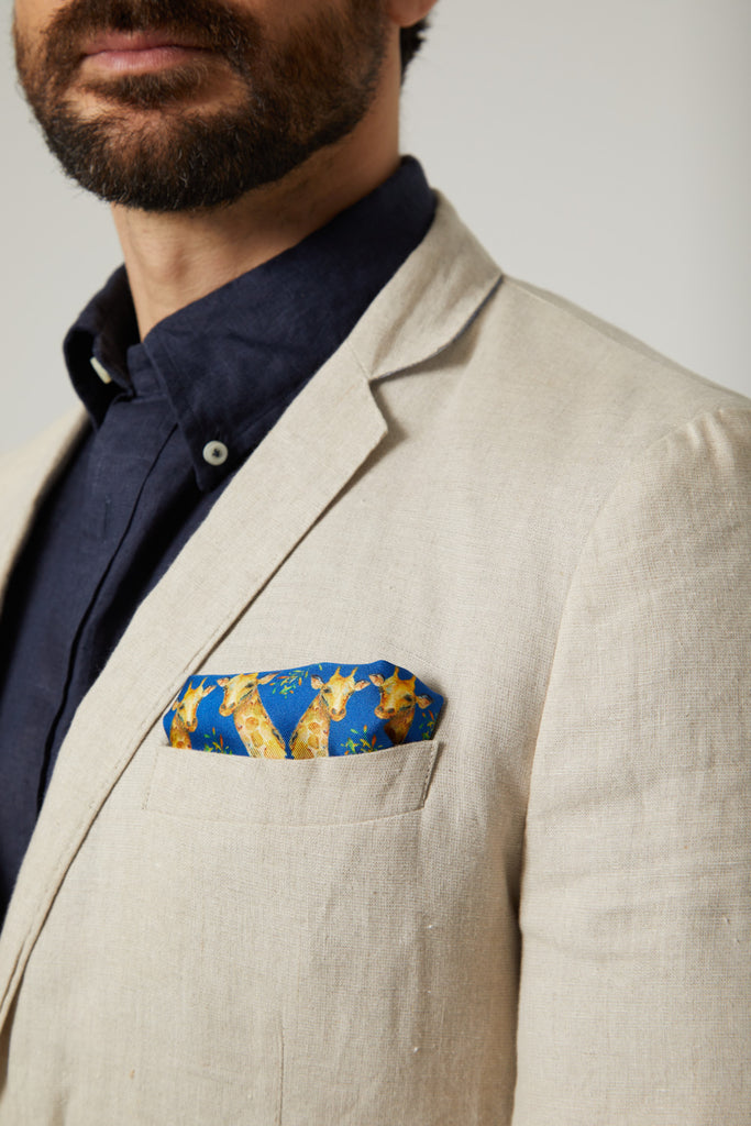 Detalle hombre con chaqueta beige y pañuelo de bolsillo de seda natural azul con jirafas