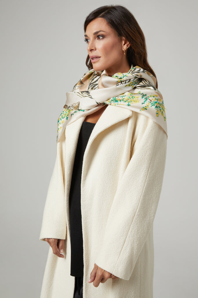Mujer elegante con abrigo blanco y pañuelo de seda natural crudo con cebras y flores verdes y amarillas