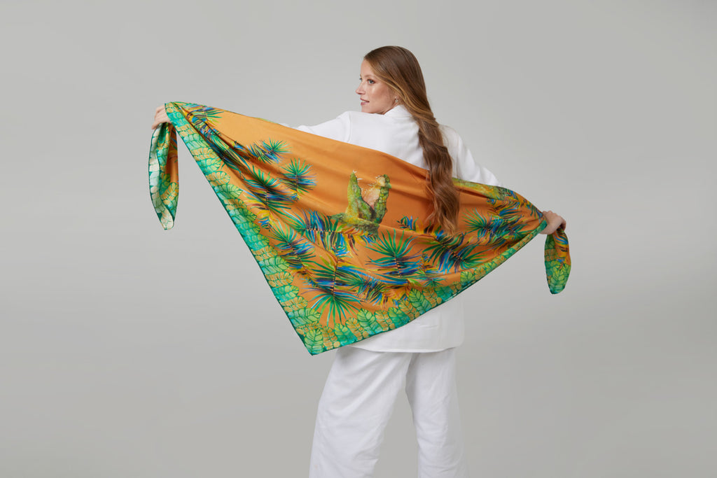 Mujer elegante con pañuelo de seda natural maxi abierto a modo de mantón con colores naranjas y verdes y diseños de hojas y cocodrilos