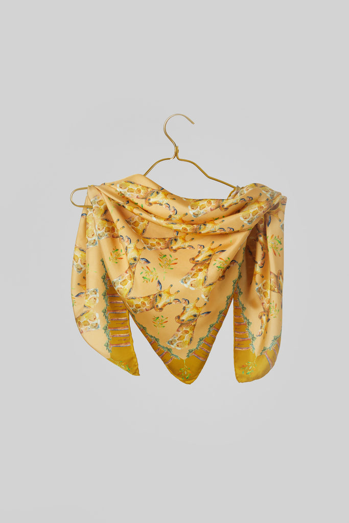 Pañuelo de seda amarillo con jirafas y bao babs sobre percha